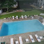 Outdoor swimming pool area at night with lounge chairs and city background.