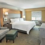 Modern hotel room with a large bed, comfortable armchair, and workspace.