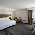 Spacious hotel room with a large white bed, modern decor, and city view.