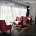 Lounge area with red armchairs by large, sheer-curtained windows.