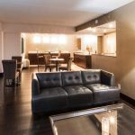 Modern hotel suite living area with dark leather sofa, dining space, and contemporary lighting.