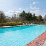 Blue swimming pool surrounded by lounge chairs and trees under a bright, partly cloudy sky.