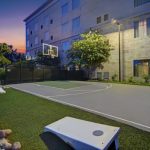 Outdoor basketball court and green space next to a modern apartment building at dusk.
