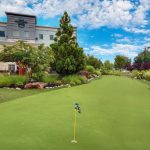 Putting green in front of a hotel with lush landscaping and blue sky.