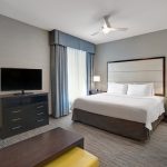 Modern hotel room with king bed, dresser, and large TV.