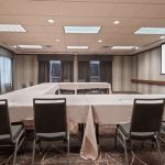 Conference room setup with tables and chairs, featuring a projector screen displaying Homewood Suites by Hilton.