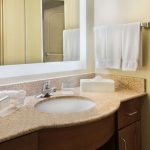 Bathroom vanity with beige countertop, sink, mirror, and white towels.