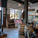 Rustic brewery interior with exposed beams, large windows, and wooden barrels.