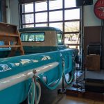 Vintage turquoise truck inside a warehouse with large industrial windows.