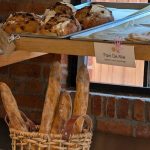 Assortment of artisanal breads displayed in a shop window, with baguettes below.