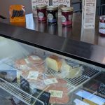 Assortment of Maine Crisp jams and cheeses displayed on a metal counter.