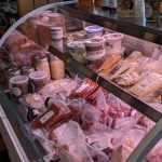 Refrigerated display case filled with various cuts of raw meat and packaged deli items.