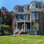 Historic Victorian mansion with dark brick, American flag flying, and a museum sign.