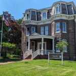 Historic Victorian mansion with dark brick and dormer windows, featuring a porch.