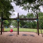 Wooden outdoor jungle gym structure in a grassy park setting under an overcast sky.