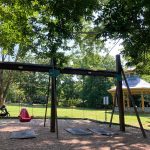 Outdoor yoga setup under trees with wooden frame, mat, and red ball in a park.