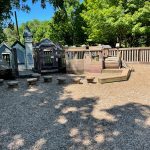 Playground structure with wooden fort and climbing area under green trees.