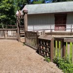Wooden boardwalk and cabin with porch under green trees.