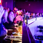 Crowd enjoying a lively indoor event with stage lighting and bar area.