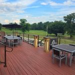 Red wooden deck overlooking a green golf course under a blue, cloudy sky.