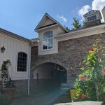 Stone and siding house with arched entryway under a bright blue sky.