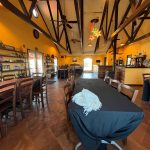 Rustic dining hall with exposed beams, terracotta floors, and long tables set for a gathering.