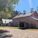 Historic red barn with white trim under a bright blue sky, surrounded by trees.