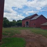 Red barns under a cloudy blue sky with green fields and trees in the background.