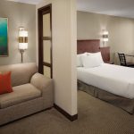 Hotel room with sofa and artwork, adjacent to a modern bedroom with a large bed.