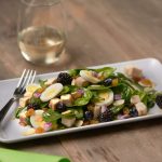 Salad with greens, eggs, blackberries, and tofu on a wooden table next to water.