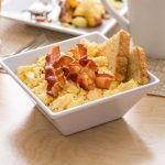 Deviled eggs with bacon and toast served on a white square dish.