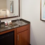 Kitchenette counter with sink, coffee maker, and toiletries in a modern room.