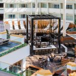 Modern hotel courtyard with outdoor seating, central fire pit structure, and terraced landscaping.