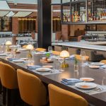 Upscale bar and dining area with long wooden table set for guests, featuring a well-stocked back bar.