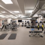 Modern gym interior with weight machines, cardio equipment, and exposed ductwork.