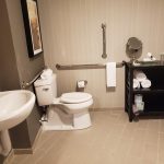 Modern hotel bathroom with white toilet, sink, and dark storage unit.