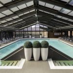 Indoor swimming pool under a glass and metal roof with lounge chairs.