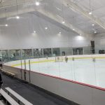 Indoor ice rink with a large, bright sheet of ice under a high, netted ceiling.
