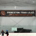 Sign for Princeton Tiger Lilies with website address displayed on a corrugated metal wall.