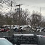 Junk pile behind a gray fence under an overcast sky with utility poles.