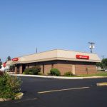 Suburban convenience store with tan siding and red branding under a clear blue sky.