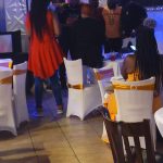 People gathered at an indoor event with a decorated backdrop and tables.