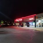 Nighttime view of a strip mall featuring "Sticky Wicket" and Boost mobile stores.