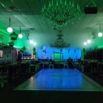 Large event hall with a central dance floor, green lighting, and chandeliers.