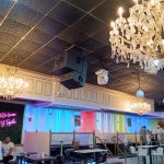 Elegant restaurant interior with crystal chandeliers, blue and pink lighting, and dining tables.