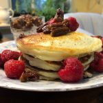 Stack of pancakes topped with berries and pecans, served on a blue and white plate.
