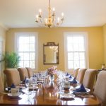 Elegant dining room with wooden table set for a meal, chandelier overhead.