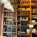 Wooden shelving unit stocked with jars of spices, preserves, and gourmet goods in a rustic store setting.