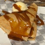 Stack of crepes drizzled with caramel sauce and topped with vanilla ice cream.