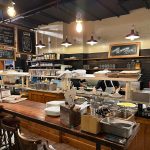 Rustic cafe interior with wooden counters, coffee bar setup, and warm overhead lighting.